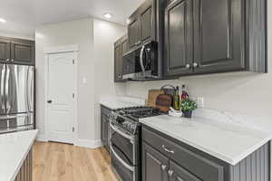 Kitchen with light stone countertops, stainless steel appliances, and light wood-type flooring