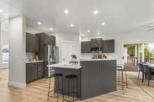 Kitchen featuring dark brown cabinetry, a kitchen island with sink, light hardwood / wood-style flooring, stainless steel appliances, and a breakfast bar area