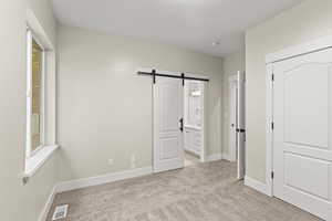 Bedroom #3  featuring a barn door, connected bathroom, sink, and light carpet