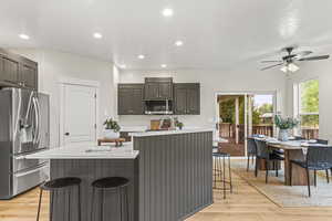 Kitchen with ceiling fan, an island with sink, light hardwood / wood-style flooring, stainless steel appliances, and a breakfast bar area