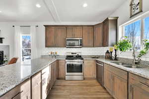 Kitchen featuring decorative backsplash, sink, light stone countertops, and stainless steel appliances