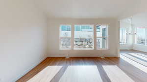 Spare room with an inviting chandelier, light hardwood / wood-style flooring, and vaulted ceiling