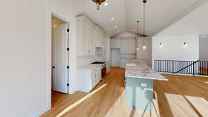 Kitchen with a center island with sink, white cabinets, hanging light fixtures, vaulted ceiling, and light stone countertops