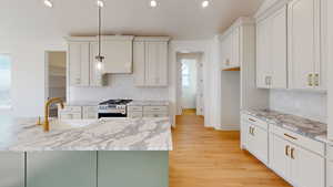 Kitchen with white cabinets, sink, light hardwood / wood-style flooring, tasteful backsplash, and decorative light fixtures