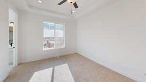 Carpeted spare room featuring ceiling fan and a tray ceiling