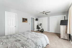 Carpeted bedroom featuring two closets, ceiling fan, and a textured ceiling