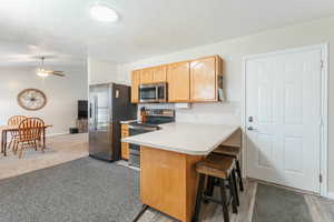 Kitchen featuring appliances with stainless steel finishes, a breakfast bar, kitchen peninsula, ceiling fan, and light colored carpet