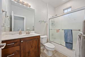 Full bathroom with shower / bath combination with glass door, vanity, toilet, and tile patterned floors