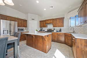 Kitchen with appliances with stainless steel finishes, backsplash, a kitchen island, light tile patterned floors, and sink