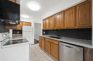 Kitchen with light tile patterned flooring, sink, white appliances, a textured ceiling, and decorative backsplash