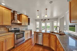 Kitchen with wall chimney range hood, light stone counters, sink, appliances with stainless steel finishes, and light hardwood / wood-style floors