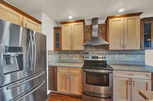 Kitchen with wall chimney range hood, light stone countertops, stainless steel appliances, and tasteful backsplash