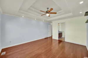 Unfurnished bedroom with ensuite bath, dark hardwood / wood-style floors, ceiling fan, and a tray ceiling