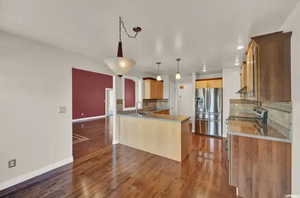 Kitchen featuring dark wood-type flooring, kitchen peninsula, decorative backsplash, and stainless steel refrigerator with ice dispenser