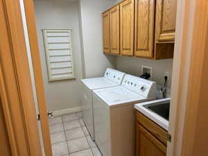 Laundry area featuring light tile patterned floors, sink, cabinets, and washing machine and dryer