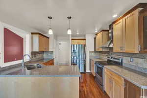 Kitchen featuring light stone countertops, stainless steel appliances, sink, wall chimney range hood, and dark hardwood / wood-style floors