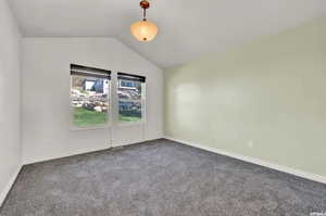 Carpeted spare room featuring vaulted ceiling