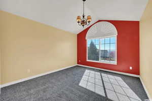 Spare room with carpet floors, a chandelier, and vaulted ceiling