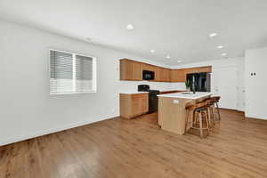 Kitchen featuring light hardwood / wood-style floors, sink, a kitchen bar, a kitchen island, and black appliances