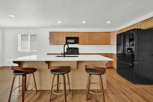 Kitchen with an island with sink, light wood-type flooring, black appliances, and sink