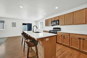 Kitchen featuring light hardwood / wood-style floors, sink, an island with sink, a kitchen bar, and black appliances