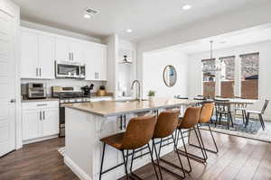 Kitchen featuring pendant lighting, white cabinets, a center island with sink, appliances with stainless steel finishes, and dark hardwood / wood-style flooring