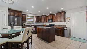 Kitchen with dark brown cabinets, black appliances, a center island, and light tile patterned floors