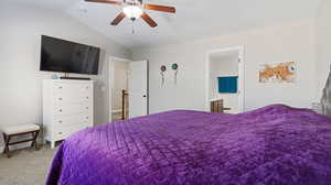 Carpeted bedroom with ceiling fan, vaulted ceiling, and ensuite bathroom