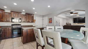 Kitchen featuring ceiling fan, light tile patterned floors, black appliances, a center island, and dark stone countertops