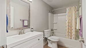 Full bathroom featuring vanity, shower / bath combination with curtain, a textured ceiling, hardwood / wood-style flooring, and toilet