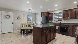 Kitchen with light tile patterned floors, sink, a kitchen island, stainless steel refrigerator with ice dispenser, and black dishwasher