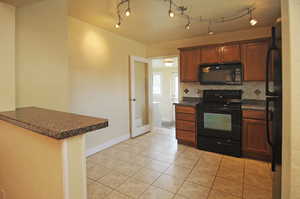 Kitchen with black appliances, kitchen peninsula, track lighting, and tasteful backsplash