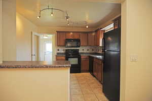 Kitchen with light tile patterned floors, kitchen peninsula, decorative backsplash, and black appliances