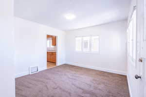 Unfurnished bedroom featuring a textured ceiling, ensuite bathroom, and light colored carpet