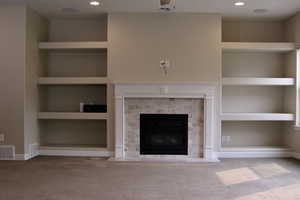 Unfurnished living room with built in shelves, carpet floors, and a brick fireplace