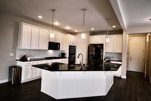 Kitchen featuring an island with sink, hanging light fixtures, dark hardwood / wood-style floors, and black appliances