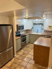 Kitchen with sink, white cabinets, green cabinetry, backsplash, and appliances with stainless steel finishes