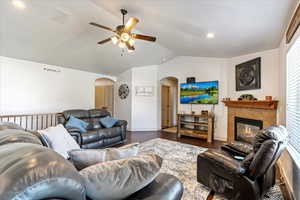 Living room featuring vaulted ceiling, ceiling fan, a tiled fireplace, and dark wood-type flooring