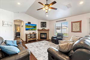 Living room with vaulted ceiling, ceiling fan, a fireplace, and dark hardwood / wood-style flooring