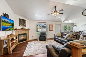 Living room featuring ceiling fan, a tiled fireplace, vaulted ceiling, and dark hardwood / wood-style flooring