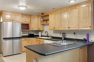 Kitchen with light brown cabinetry, a textured ceiling, and stainless steel fridge