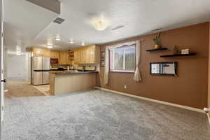 Kitchen featuring a textured ceiling, kitchen peninsula, light brown cabinetry, and stainless steel fridge