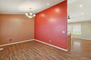 Unfurnished room featuring ceiling fan with notable chandelier and dark wood-type flooring