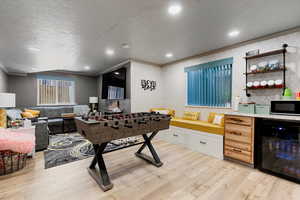 Playroom with a textured ceiling, light hardwood / wood-style floors, ornamental molding, and beverage cooler