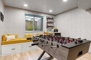 Recreation room featuring a textured ceiling, light wood-type flooring, and crown molding