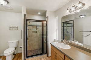 Bathroom featuring wood-type flooring, walk in shower, vanity, and toilet