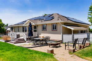 Back of house with a lawn, solar panels, a wooden deck, and a patio area