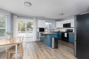 Kitchen with blue cabinets, butcher block countertops, white cabinetry, appliances with stainless steel finishes, and a breakfast bar