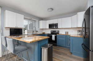 Kitchen featuring blue cabinets, butcher block counters, appliances with stainless steel finishes, and white cabinetry