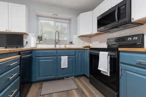 Kitchen with black electric range oven, blue cabinets, dark wood-type flooring, and white cabinets